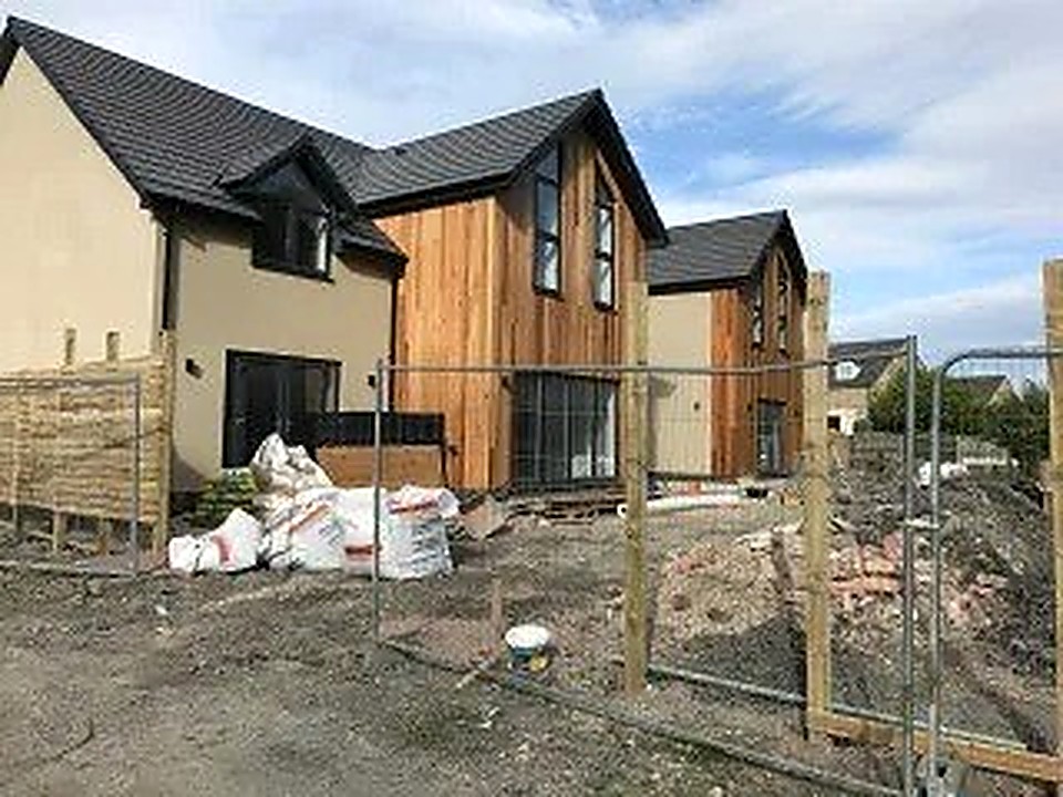 Timber-clad contemporary new build homes behind site fencing during construction in Derbyshire