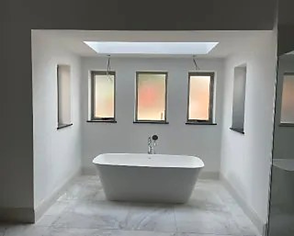 Freestanding bath beneath a skylight and slim vertical windows in a Derbyshire bathroom
