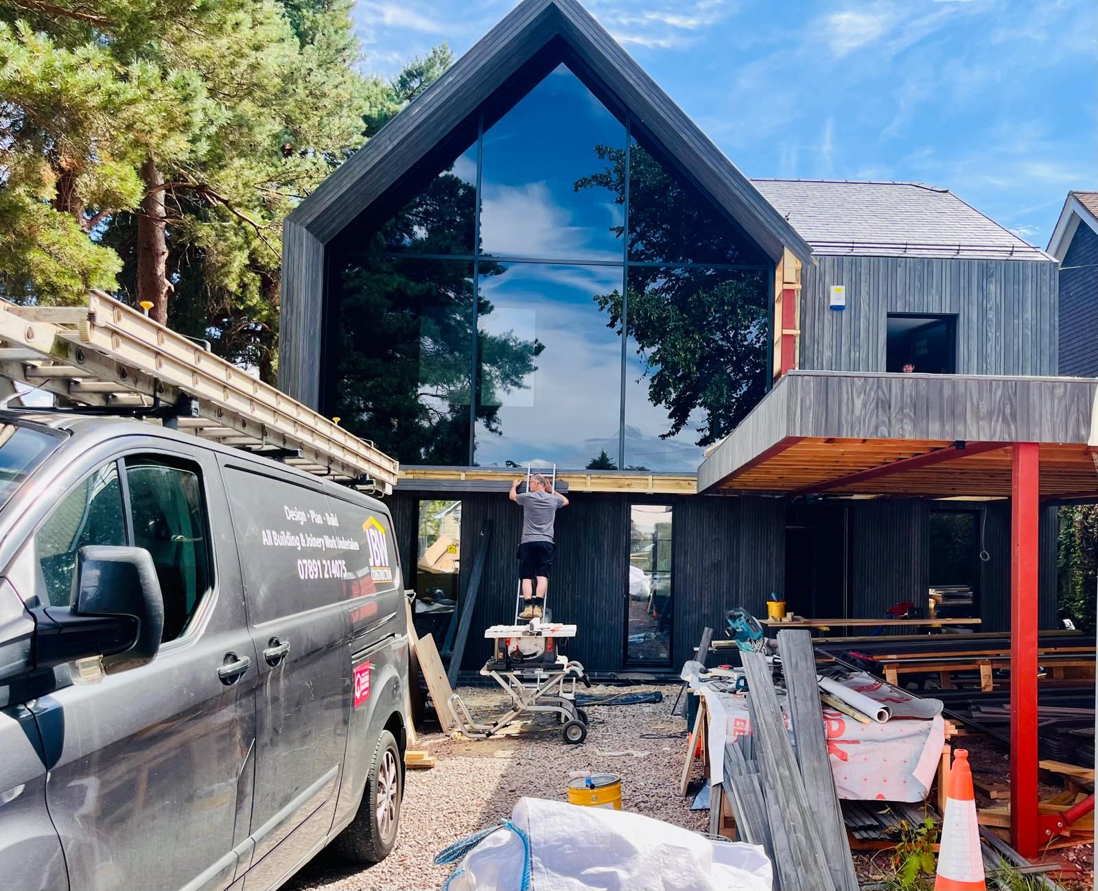 Charred timber-clad architect-designed home mid-construction with cladding being fixed to the gable, Derbyshire